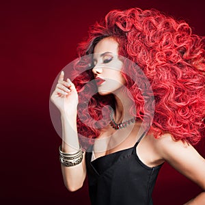 Portrait of a young attractive woman with a very lush hairstyle. Red hair on a red background.