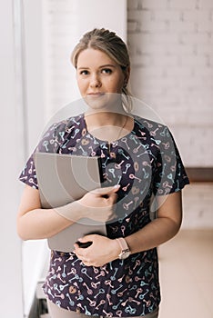 Portrait of young attractive woman wearing casual clothing holding folders while standing in office