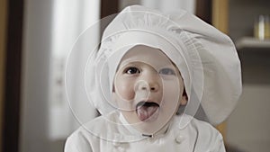 portrait of Young baby chef makes the tongue to the camera. Child with toque blanche makes funny faces.