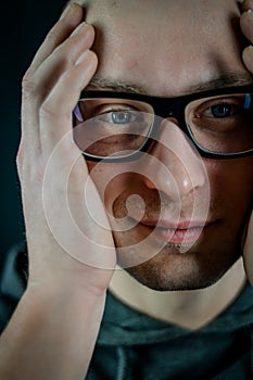 Portrait of a young bald man with black eyeglasses holding his head in his hands