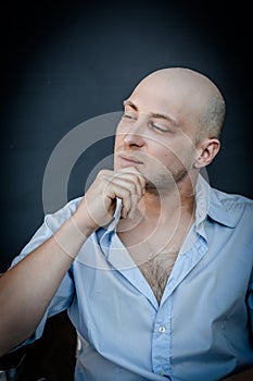 Portrait of a young bald man holding his chin with his hand and looking thoughtful as he looks away