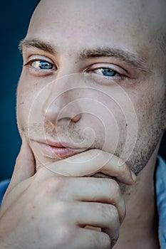Portrait of a young bald man holding his chin with his hand and looking thoughtful as he looks in front of him