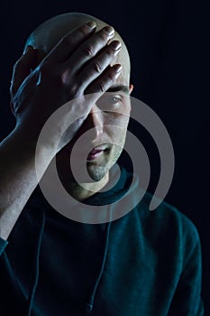 Portrait of a young bald man who partially covers his face with his hand on his forehead and looks sad