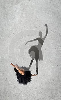 Portrait of young ballerina in black dress performing isolated over grey wall background. Top view. Shadow element