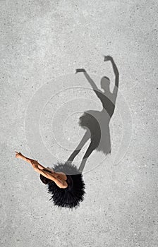 Portrait of young ballerina in black dress performing isolated over grey wall background. Top view. Shadow element