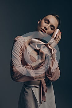 Portrait of young ballerina with closed eyes holding pointe shoes in her hands