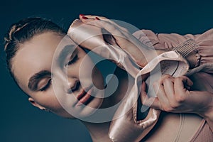 Portrait of young ballerina with closed eyes holding pointe shoes in her hands