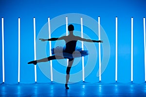 Portrait of a young ballerina on pointe shoes in a white tutu against background of bright blue neon lights. A young