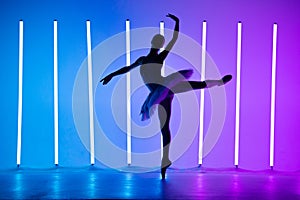 Portrait of a young ballerina on pointe shoes in a white tutu against background of bright neon lights. A young graceful