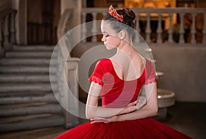 Portrait of young ballerina in a red tutu and crown from back, face turned in profile against the background of vintage interior