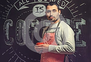 Portrait of a young baristas in a red apron with a cup in the ha