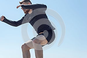 Portrait of a young bearded athlete of twenty-five, jumping against a blue sky.