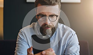 Portrait of young bearded attractive businessman in shirt and glasses using smartphone, working. Hipster man is chatting