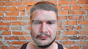 Portrait of young bearded guy looking into camera with confident and serious expression on his face outdoor. Close up of