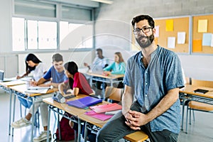 Portrait of young bearded male teacher sitting at high school table