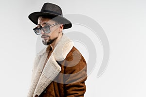 Portrait of young bearded man in black hat and brown coat in black sunglasses isolated over white background, copyspace