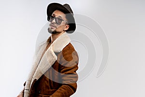 Portrait of young bearded man in black hat and brown coat in black sunglasses isolated over white background, copyspace