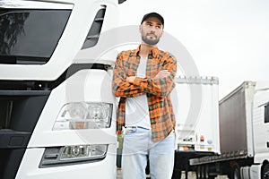 Portrait of young bearded man standing by his truck. Professional truck driver standing by semi truck vehicle.
