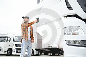 Portrait of young bearded man standing by his truck. Professional truck driver standing by semi truck vehicle.