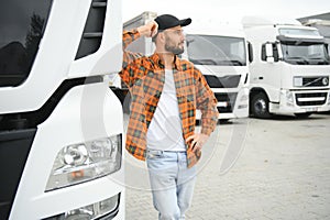 Portrait of young bearded man standing by his truck. Professional truck driver standing by semi truck vehicle.