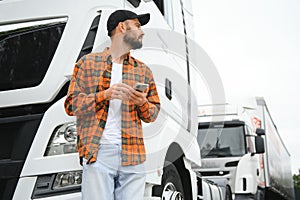 Portrait of young bearded man standing by his truck. Professional truck driver standing by semi truck vehicle.