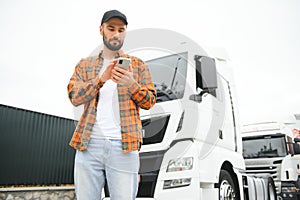 Portrait of young bearded man standing by his truck. Professional truck driver standing by semi truck vehicle.