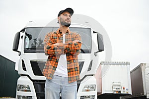 Portrait of young bearded man standing by his truck. Professional truck driver standing by semi truck vehicle.