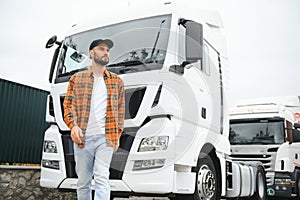 Portrait of young bearded man standing by his truck. Professional truck driver standing by semi truck vehicle.