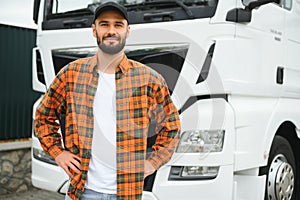 Portrait of young bearded man standing by his truck. Professional truck driver standing by semi truck vehicle.