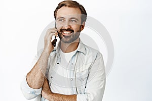 Portrait of young bearded man talking on mobile phone, making telephone call, standing over white background. Cellular