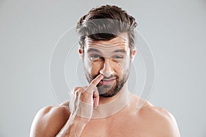 Portrait of a young bearded naked man picking his nose