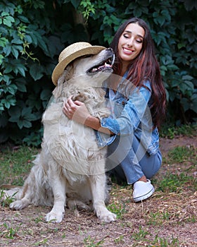 Portrait of young beautiful 30 year old woman with her funny playing pet dog Golden retriever wearing a hat.