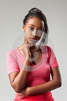 Portrait of young, beautiful african girl in pink clothes posing against grey studio background. Deep attentive look at