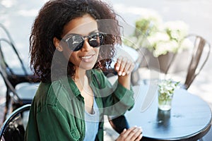 Portrait of young beautiful african girl in sungasses smiling resting relaxing in cafe on terrace.