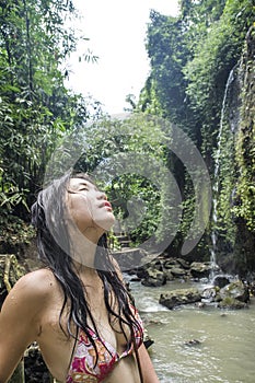 Portrait of young beautiful Asian girl looking pure and enjoying nature beauty with face wet under amazing beautiful natural water