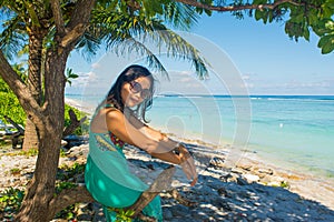 Portrait of young beautiful asian girl sitting in shade under the tree on tropical beach looking at camera