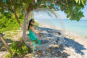 Portrait of young beautiful asian girl sitting in shade under the tree on tropical beach looking a side