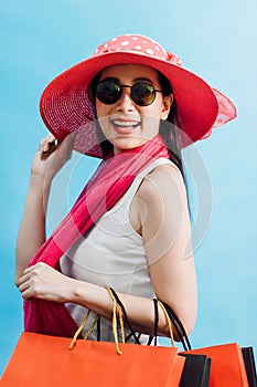 Portrait of young beautiful asian girl wearing white lady vest, sunglasses and sun hat holding shopping bags