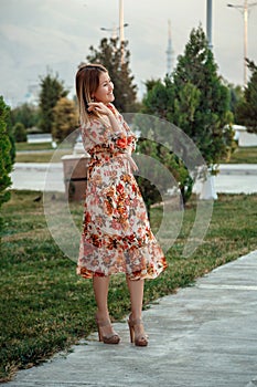 Portrait of a young beautiful Asian skinny slender woman in a floral print dress standing outside during sunset