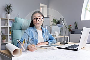 Portrait of a young beautiful Asian woman architect working at a computer and drawing on a project