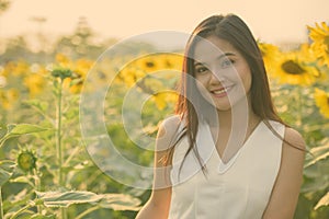 Young happy beautiful Asian woman smiling in the field of blooming sunflowers