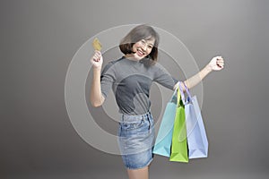 Portrait of young beautiful asian woman holding credit card and colorful shopping bag isolated over gray background studio