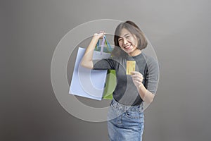 Portrait of young beautiful asian woman holding credit card and colorful shopping bag isolated over gray background studio