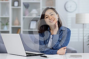 Portrait of young beautiful asian woman at home, woman smiling and looking at camera, working remotely in home office