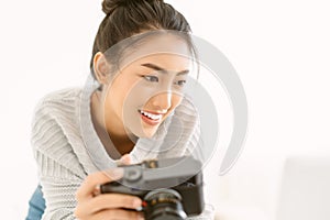 Portrait of young beautiful Asian woman photographer with her professional camera and check photo on laptop computer in home