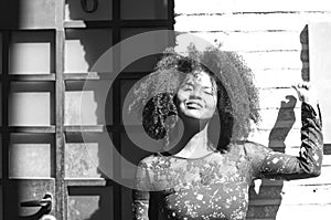 Portrait of young, beautiful black woman with afro hair and black dress with flowers is leaning against the wall of a building in