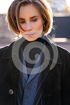 Young blond short-haired woman in velvet coat, vest and sweater on sunny street