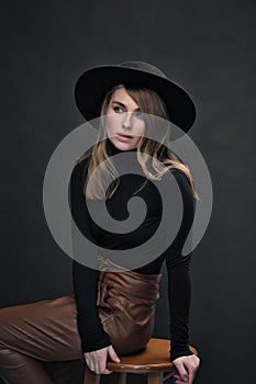 Portrait of young beautiful blond woman with light makeup and blue eyes touching her face. Dark background. Black tight