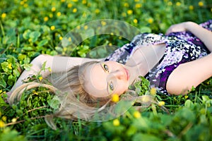 Portrait of young beautiful blond woman lying in grass and flowers on summer day with green nature landscape