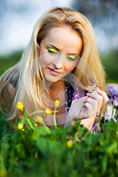 Portrait of young beautiful blond woman lying in grass and flowers on summer day with green nature landscape